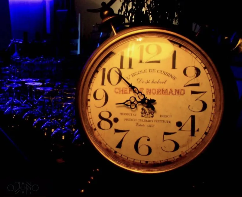 A lit vintage clock standing in front of a row of blue glasses.