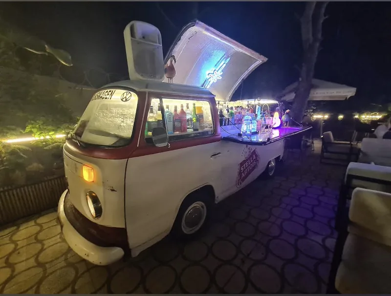A Volkswagen Combi turned into a bar, lit up on the terrace at night.